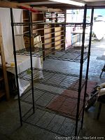 Full view of the shelving unit in an indoor space showing four wire shelves and black metal frame.