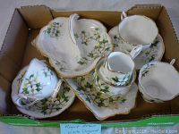Box containing Royal Albert Dogwood pattern vintage china including teacups, saucers, creamer, and small plates all decorated with white dogwood flowers and gold trim.