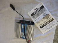 Power 500 watt DC to AC power inverter unit with attached cable laid on fabric surface alongside the owner's manual.