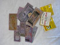 Collection of assorted vintage/antique banknotes and three beer label stickers on a white fabric background.