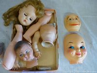 Photo showing assortment of vintage doll heads, limbs and torso in a box.
