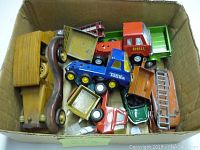 Box containing a variety of vintage toy cars and trucks including metal and wooden pieces in assorted colors.
