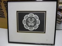 Framed First Nations print with central circular face motif and surrounding shapes on black background, showing full framed artwork.
