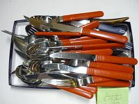 Photo of assorted vintage cutlery with orange handles, showing multiple forks, knives, and spoons stacked together in a tray.