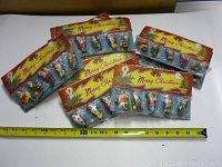 Ten vintage packages of Christmas gnome tree ornaments laid out together with a measuring tape indicating approximately 8 inches width per package.