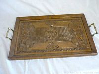 Overview of the entire carved oak serving tray showing the wooden surface, carved details, and brass handles on both ends.