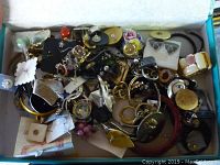 Box of loose vintage costume jewelry with mixed types including earrings, rings, bracelets, brooches, and necklaces shown from a top angle