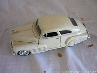 Off-white 1:24 scale diecast model of 1948 Chevrolet Aero Sedan car, shown angled left side view on neutral backdrop.
