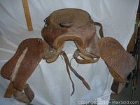 Front angled view of the worn leather Western saddle showing embossed designs and paint spill on the left skirt.