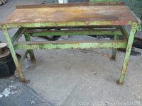 Front view of steel workbench showing green painted angle iron frame with surface rust and welded construction