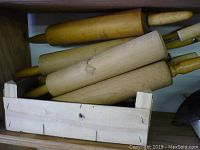 Seven wooden rolling pins displayed in two boxes with various sizes and handle styles visible, natural wood tones with some wear marks.