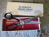 Pair of Kleencut pinking shears with black handles and serrated blades shown open on top of original Kleencut box with branding text.