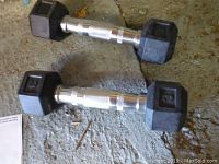 Two 3 pound hex dumbbells laid on rough concrete surface, showing rubber-coated ends and knurled chrome handles for grip.