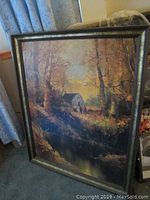Large framed painting of a rural scene with a house, trees, and a stream, showing warm autumn colors.