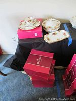 Stack of Royal Albert red boxes, a place setting and serving pieces on black cloth
