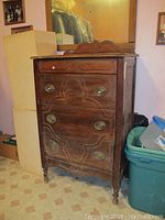 Wooden dresser with three drawers, decorative carved wood pattern, oval brass pulls, and mildew wear visible on top and sides.
