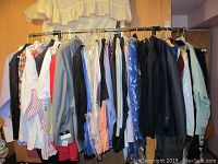 Garment rack holding multiple men's dress shirts and suits, some covered in plastic garment bags.
