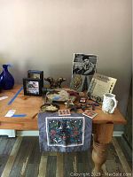 Photo showing multiple items on wooden table including brass dog head bookends, handmade mug, star art, coasters, marble platter, photo of Elvis Presley, and shadow box art.