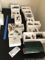Overview photo of Department 56 Heritage Village and Alpine Villagers collection items displayed on table including boxed and tray-stored porcelain figurines and accessories.