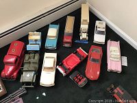 Photo of 12 James B Beam Distilling Co collectible car and truck decanters displayed on carpet, showing variety of vehicle types including cars, jeep, golf cart, trucks, and police car.