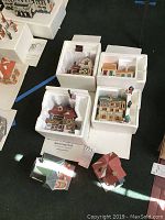 Image showing six miniature buildings in foam packaging on black carpet, including various detailed Dickens Village structures.