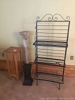 Photo showing the black metal bakers rack, wooden plant stand, and two column plant stands in a row against a wall.