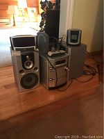 Photo showing Sony stereo system with two silver and black large speakers, remote control on stereo top, small CRT TV or monitor on one speaker, and Timex clock radio on second speaker.