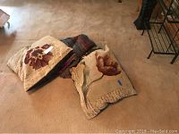 Two floral decorative pillows and Ecuadorian woven blankets spread on carpet.