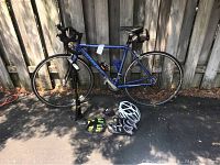 Blue Trek High Road Cycle road bike standing against fence with JoeBlow pump to the left, helmet, gloves, and cycling shoes on pavement in front.
