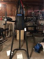 Front view of the Fitness Gear Power Tower showing padded back support, arm rests, pull-up bar, and dip handles. Manual visible on floor.