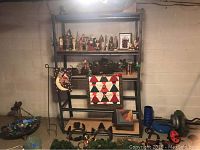 Photo showing metal shelving unit with multiple Christmas Santa figurines on top shelf and a patterned fabric wall hanging in the center shelf.