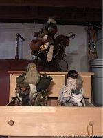 Photo showing two Santa Claus figurines standing side by side, one holding a green bag and the other holding a small tree, with detailed cloth and fabric beards.