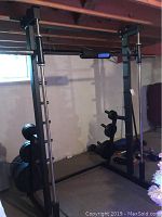 Full view of the black metal power lifting rack with barbell and weight plates on side storage posts.