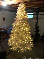 White artificial Christmas tree illuminated with warm white lights, set up in basement space.