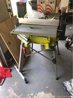 Ryobi 10 inch table saw on its stand with safety guard, showing overall condition and configuration.