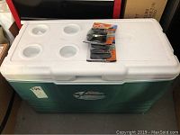 Overview photo of the green and white Coleman Ultimate Xtreme cooler with four cup holders on lid, cooler closed with two packages of Homax Cinchite tarp clips on top.