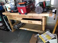 Front view of wooden work bench showing 4 drawers, lower shelf, and items on top