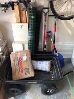 Plastic garden wagon visible with garden waste bags, fiberglass insulation, deer guard netting, snow shovels, tires closeup.