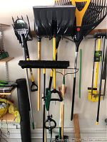 Photo showing various garden tools hanging on a wall including shovels, rakes, snow shovel and a push broom.