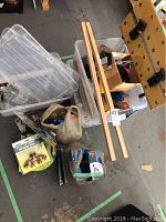 Plastic storage containers, two pieces of wooden planks, plastic bag with hardware, and various tools on the floor