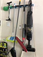 Full view of the cleaning supplies hanging on wall including vacuum, mops, broom, and pump