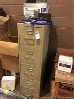 Full view of beige metal 4-drawer file cabinet in basement setting, with some boxes around it.