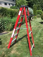 Photo of 6 feet tall red metal step ladder outdoors, showing full structure including black plastic top tray and support braces.