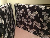 Box spring and mattress with black background and white floral pattern standing upright against a wall.