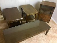 Four wood tables in room: two dark wood side tables, one long dark wood coffee table with glass top, one medium wood side table with shelving and glass front panel