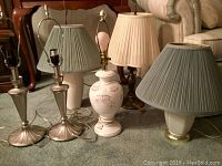 Five assorted lamps shown on carpeted floor in front of furniture, varied styles and shades.
