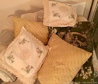 Photo of six decorative pillows arranged on a chair including floral embroidered, yellow textured, and green floral designs