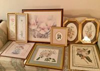 Eight assorted framed flower pictures displayed on a couch and floor, various frame sizes and colors.