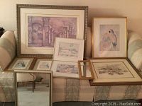 View of six framed pictures and two mirrors placed on a couch, showing different artistic themes and frame styles.