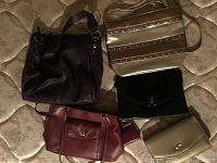 Top-down view of four purses arranged on patterned mattress: dark brown handbag (top left), gold/silver striped crossbody (top right), black velvet clutch (bottom right), burgundy shoulder bag (bottom left), plus a small gold pouch near the clutch.
